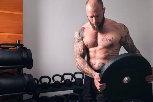 sportsman with muscular body and naked torso standing with heavy weight plate during workout in gym, concept of fitness and active lifestyle