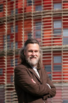 positive middle age male with beard in elegant suit standing with arms crossed and looking at camera against urban building, concept of business and mature man lifestyle, copyspace for text