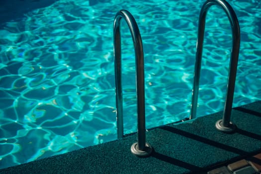 A metal ladder is in the water. The water is clear and calm. The ladder is in the middle of the pool