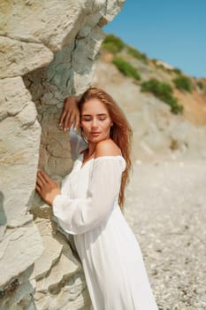 A woman in a white dress is standing on a rocky beach. Concept of serenity and tranquility, as the woman is enjoying the natural beauty of the beach
