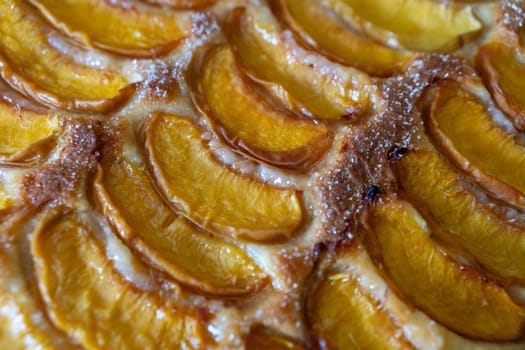 A dessert made of sliced peaches is on a wooden cutting board. The dessert is covered in sugar and looks delicious