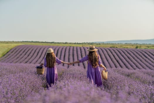 Mom and daughter are running through a lavender field dressed in purple dresses, long hair flowing and wearing hats. The field is full of purple flowers and the sky is clear