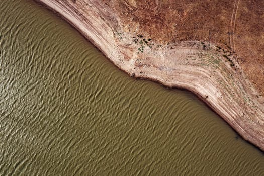 drone view of river with rippled water surface flowing near stony shore with dried surface in nature, concept of environment and ecology