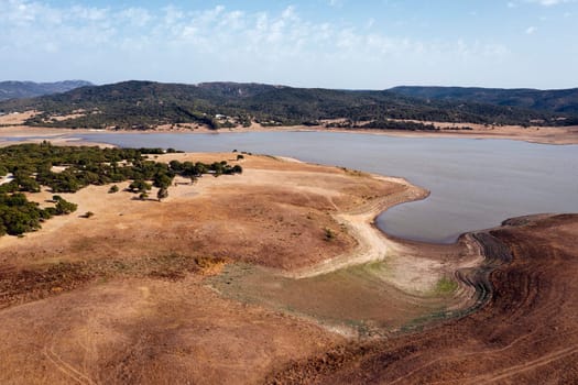 dry barren landscape with a lake in the distance, the water is muddy and the land is brown and dry, concept of peaceful and serene landscape in the vast expanse of terrain