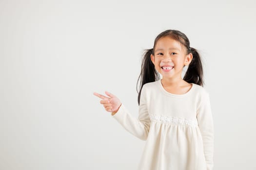 Happy Asian portrait cute young kid girl smiling indicate finger empty space, studio shot isolated on white background, Thai kindergarten child pointing index out with copy space