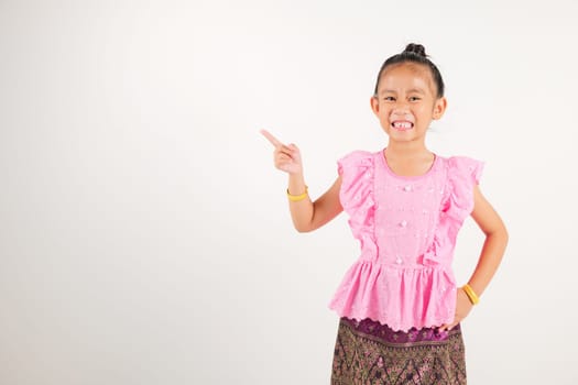 Portrait Thailand kid girl smiling traditional Thai dress costume indicate finger empty space, studio isolated white background, kindergarten child pointing index out with copy space