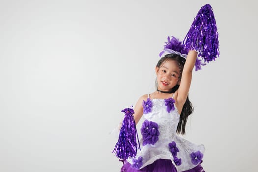 Little girl in cheerleading outfit with purple pom-poms, beaming happily in a white studio setup. A moment of fun and energy. cheerleader kid