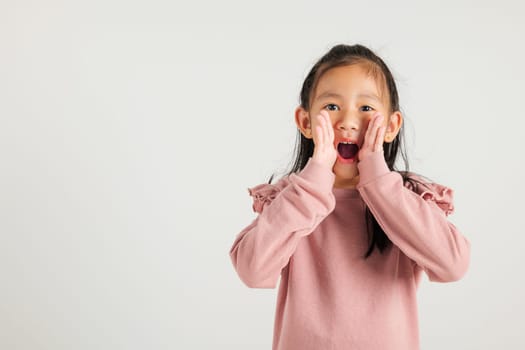 Asian happy portrait cute young kid girl standing hand on mouth talking news announcement studio shot isolated on white background, Thai kindergarten child announcement
