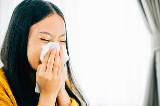 In an apartment a woman holds a tissue covering her nose due to coughing and sneezing. Portrait of a worried patient managing illness. Snot and handkerchief in hand.
