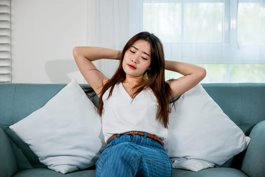 Happy woman feeling relax comfortable enjoying after homework, Asian young female enjoying free time relaxing put arm hand back behind head sitting on sofa in living room at home
