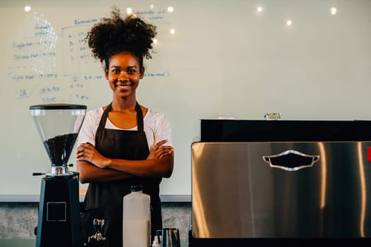 In the cafe a confident black woman stands at the counter. Portrait of owner a successful businesswoman in uniform smiling with satisfaction ensuring customer service. Inside a small business cafe