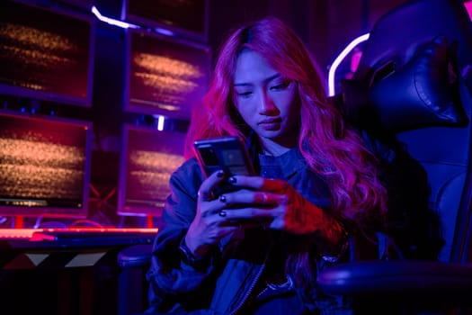 Asian woman in front of a computer monitor display using mobile phone, neon light, Hacker wear black jacket at system control room, Security guard working on multiple monitors together smartphone