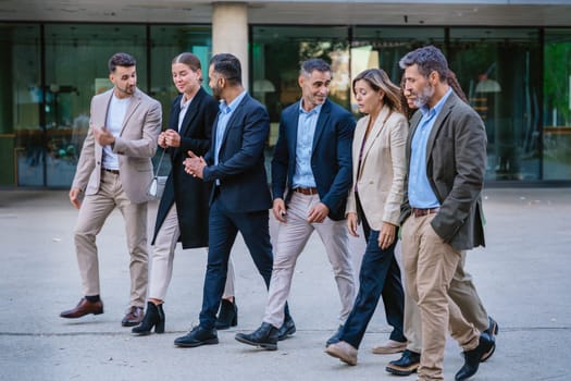 A diverse group of business professionals walking together outside a modern office building. They are engaged in conversation, dressed in formal and smart casual attire.