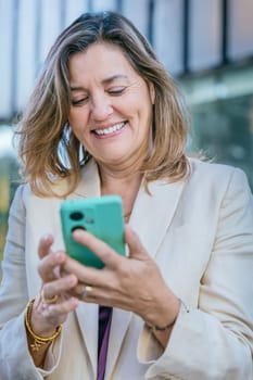 Smiling middle-aged businesswoman using a smartphone outdoors in a modern urban setting.