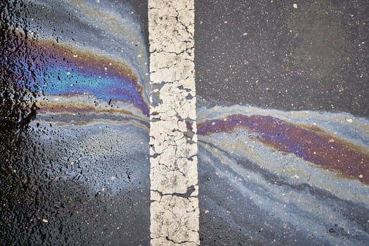 Gasoline or oil polluting wet asphalt road creating rainbow pattern next to a white dividing line.