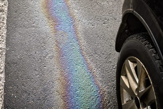 Gasoline or oil spill creating rainbow sheen on asphalt parking lot next to car tire
