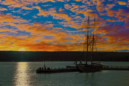 Two-masted brig at the pier under red clouds in the gathering dusk