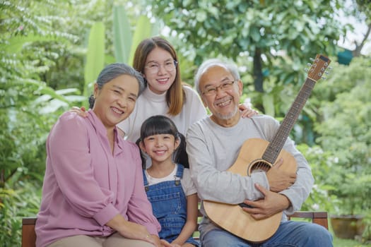 Happy family Asian senior elderly man or grandfather playing guitar while his grandmother and granddaughter singing song together outdoors at home, Activity family, Enjoying lifestyle senior older