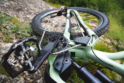 A mountain bike lies on the mountainside. A tired bicycle lies on a stone in the grass on the side of the road