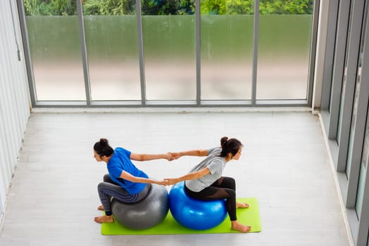 Above two Asian adult and young woman in sportswear doing aerobics yoga exercise with sitting on fitness ball indoor yoga studio, fit sport healthy workout lifestyle exercise