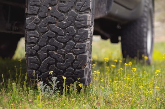 Transport, driving and car concept, close-up of a car wheel on green lush grass. A car wheel stands in the mountains in summer.