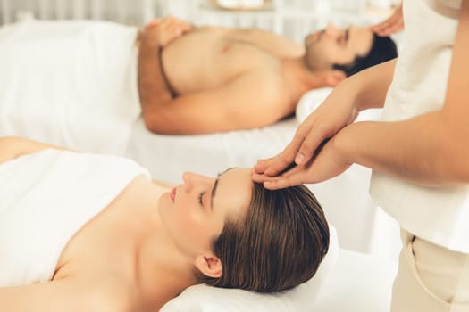 Caucasian couple enjoying relaxing anti-stress head massage and pampering facial beauty skin recreation leisure in dayspa modern light ambient at luxury resort or hotel spa salon. Quiescent