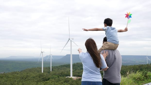 Concept of progressive happy family enjoying their time at the wind turbine farm. Electric generator from wind by wind turbine generator on the country side with hill and mountain on the horizon.