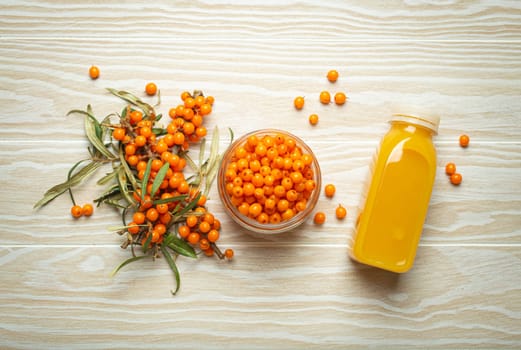 Sea buckthorn healthy drink in bottle, ripe berries in glass jar and branches with leaves top view on white wooden rustic background, great for skin, heart, vessels and immune system..