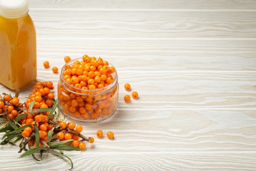 Sea buckthorn healthy drink in bottle, ripe berries in glass jar and branches with leaves top view on white wooden rustic background, great for skin, heart, vessels and immune system. Copy space..