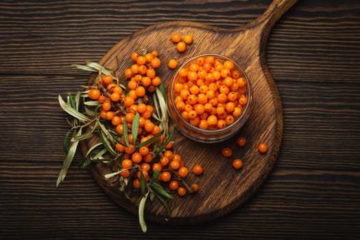 Sea buckthorn ripe berries in glass jar and branches with leaves top view on dark wooden rustic background, great for skin, heart, vessels and immune system..