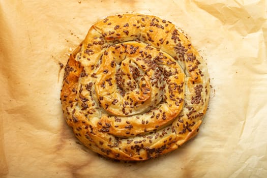 Freshly baked Burek made of filo dough with filling on baking paper background top view. Traditional savoury spiral pie of Balkans, Middle East and Central Asia.