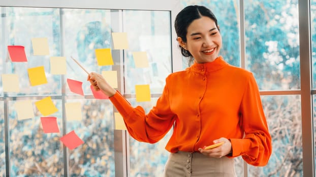 Business people work on project planning board in office and having conversation with coworker friend to analyze project development . They use sticky notes posted on glass to make it organized. Jivy