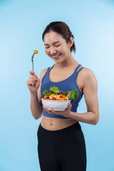 Young sporty Asian woman in sportswear holding salad bowl fill with vibrant of fruit and vegetable. Natural youthful and fit body lifestyle with balance nutrition on isolated background. Vigorous