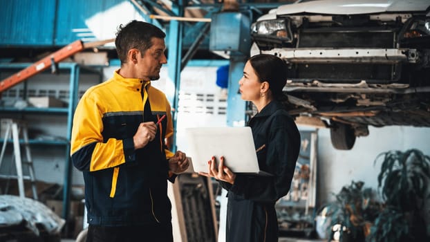 Two vehicle mechanic working together, conduct car inspection with laptop. Automotive service technician in uniform carefully make diagnostic troubleshooting to identify error. oxus