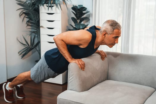 Athletic and active senior man using furniture for effective targeting muscle with push up at home exercise as concept of healthy fit body lifestyle after retirement. Clout