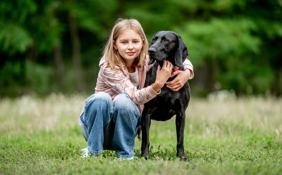 Preteen girl hugging golden retriever dog sitting at nature together. Cute child kid petting purebred pet doggy labrador in park at summer