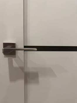 A contemporary door handle featuring a simple, linear design attached to a smooth, white door. The handle's metallic finish contrasts with the clean surface, creating an elegant look.