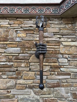 A creative wall sculpture displays a hand gripping a decorative staff, mounted on a rustic stone wall. The art piece adds character and intrigue to the setting, highlighting craftsmanship.