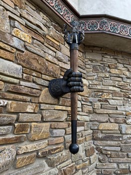 A striking wall fixture consists of a realistic hand grasping a mace, mounted on a textured stone wall. This artistic piece adds a medieval touch to the exterior design.
