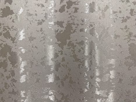 Shimmering silver fabric features a detailed textured pattern, ideal for fashion, upholstery, or decorative projects. The surface reflects light, adding depth and sophistication to any design.