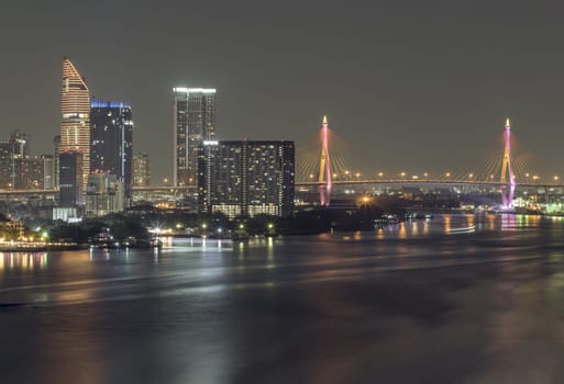 Bangkok, Thailand - Jan 10, 2025 - Nightscape city view with bright glowing lighting of Skyscrapers and Bhumibol bridge with Chao phraya river in the foreground. City scenery night of Bangkok in the sundown, use it as wallpaper, Poster and Space for text, Selective focus.