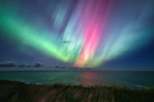 A stunning Aurora Borealis display lights up the sky over the cliffs of St. Abbs, UK. The vibrant green and pink hues of the northern lights contrast beautifully with the dark ocean and rugged coastline. A magical natural phenomenon perfect for nature, travel, and astronomy themes.