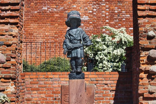 A poignant image of the Little Insurgent Monument in Warsaw, Poland. This bronze statue commemorates the children who fought in the Warsaw Uprising of 1944. The red-brick wall and greenery in the background add depth to this touching tribute.
