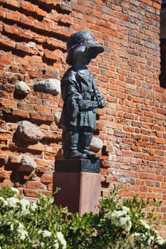 A poignant image of the Little Insurgent Monument in Warsaw, Poland. This bronze statue commemorates the children who fought in the Warsaw Uprising of 1944. The red-brick wall and greenery in the background add depth to this touching tribute.