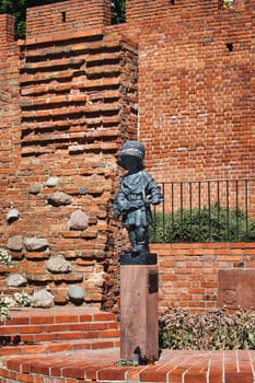 A poignant image of the Little Insurgent Monument in Warsaw, Poland. This bronze statue commemorates the children who fought in the Warsaw Uprising of 1944. The red-brick wall and greenery in the background add depth to this touching tribute.