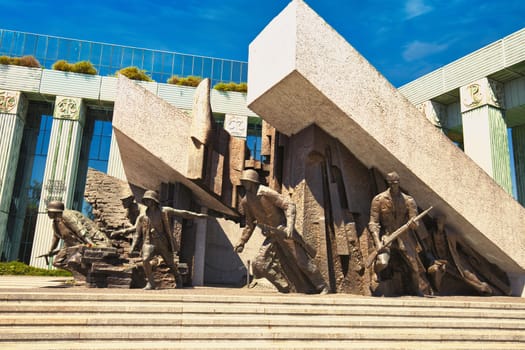 A powerful monument in Warsaw, Poland, commemorating the Warsaw Uprising of 1944. The dramatic sculpture features soldiers in action, surrounded by striking architectural elements and set against a bright blue sky. A poignant representation of courage, resilience, and history, ideal for historical and cultural themes