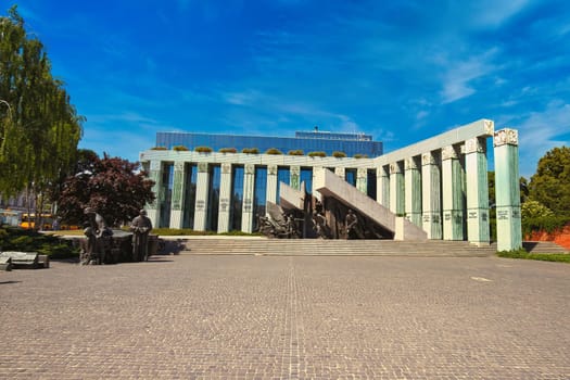 A powerful monument in Warsaw, Poland, commemorating the Warsaw Uprising of 1944. The dramatic sculpture features soldiers in action, surrounded by striking architectural elements and set against a bright blue sky. A poignant representation of courage, resilience, and history, ideal for historical and cultural themes
