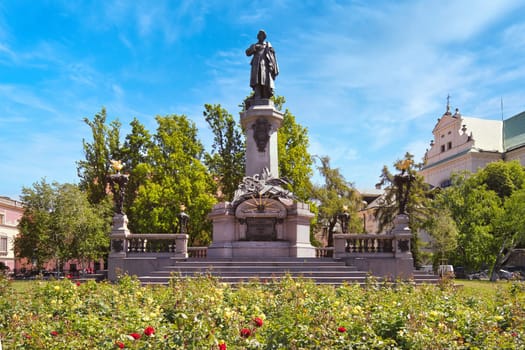 A vibrant image of the Adam Mickiewicz Monument in Warsaw, Poland, surrounded by a colorful garden and set against a bright blue sky. This statue commemorates Poland national poet and is a significant cultural landmark in the city.