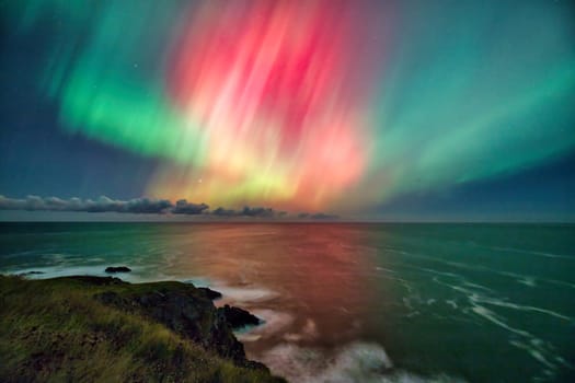 A stunning Aurora Borealis display lights up the sky over the cliffs of St. Abbs, UK. The vibrant green and pink hues of the northern lights contrast beautifully with the dark ocean and rugged coastline. A magical natural phenomenon perfect for nature, travel, and astronomy themes.