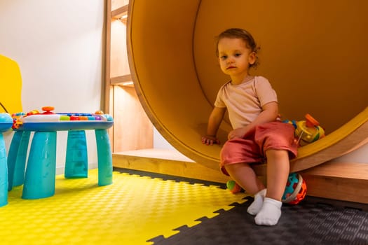 Smiling toddler playing in a vibrant playroom with interactive toys, activity tables, and colorful designs for early learning and exploration